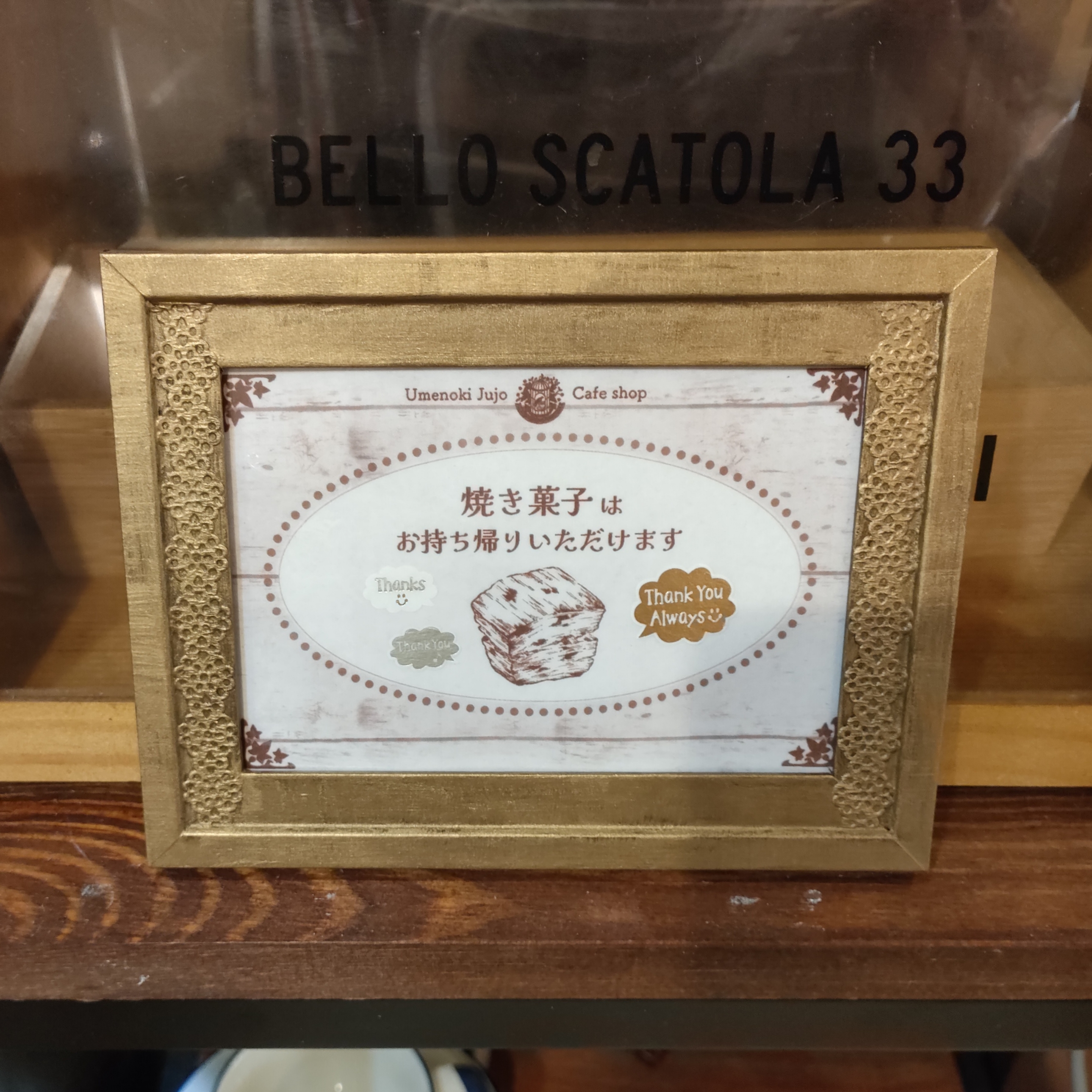(焼菓子のお持ち帰りに添えるミニチラシの画像です)(正円にアイビーの装飾を施したシンプルなエンブレム枠に、手とスコーンのペン画イラストと「梅の木十条店の焼き菓子」の文字を配置したキャッチを上部に置いて、中央に下記のテキストを白抜き背景で載せました)駅からの帰りに、いつもの喫茶店で、今日はコーヒー豆と一緒に焼き菓子を買って来た。コーヒーの湯を沸かす間に、ふと思い付いて 焼き菓子をオーブントースターで1分と少し温めてみると...　表面はカリッと、中はフワッと、まるで焼き立てのよう!贅沢なコーヒータイムに癒されたのだった。梅の木十条店 焼き菓子物語(全体背景は青色がかった明るいグレーに、コーヒーの枝をモチーフにしたシルエットとストライプを薄い白の透過を載せ、中央下部に梅の木十条店さんのロゴマークを置き、コーヒー豆の絵柄を数粒飾っています)Umenoki Jujo Cafe ShopThank you for enjoying our baked goods.